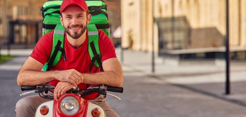 hombre con una mochila de delivery en la espalda sobre una moto estacionada