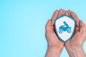 Dos manos sobre un fondo celeste con una imagen de un escudo blanco que tiene una moto en el centro